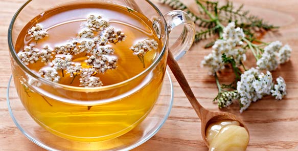 Стакан с чаем, цветы тысячелистника и ложечка мёда